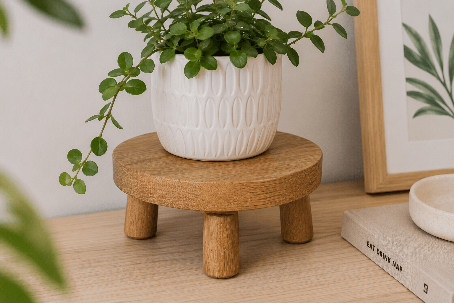 White pot with green plant on a wooden stool against a neutral wall.